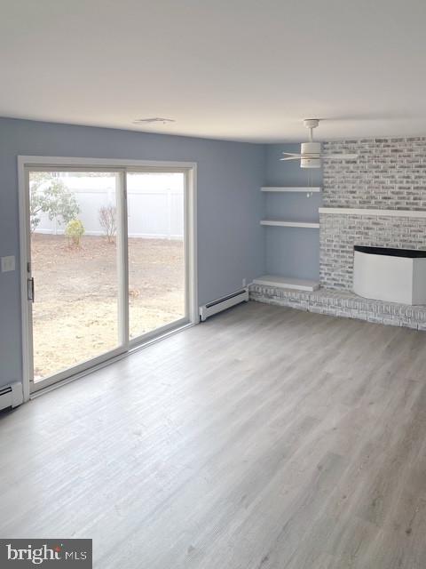 unfurnished living room with a baseboard heating unit, a fireplace, and wood finished floors