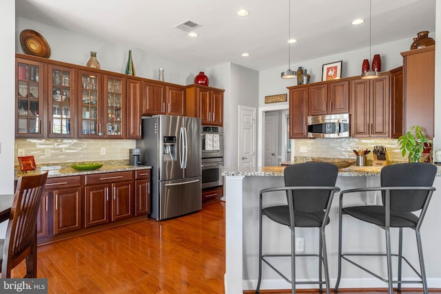 kitchen with a breakfast bar area, visible vents, appliances with stainless steel finishes, glass insert cabinets, and wood finished floors