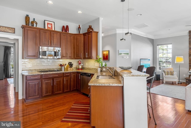 kitchen with appliances with stainless steel finishes, a breakfast bar, hardwood / wood-style floors, a peninsula, and a sink