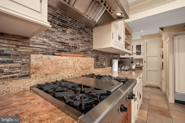 kitchen with light tile patterned floors, light stone counters, gas cooktop, custom exhaust hood, and glass insert cabinets