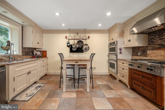 kitchen with hanging light fixtures, appliances with stainless steel finishes, light stone countertops, wall chimney exhaust hood, and a kitchen bar