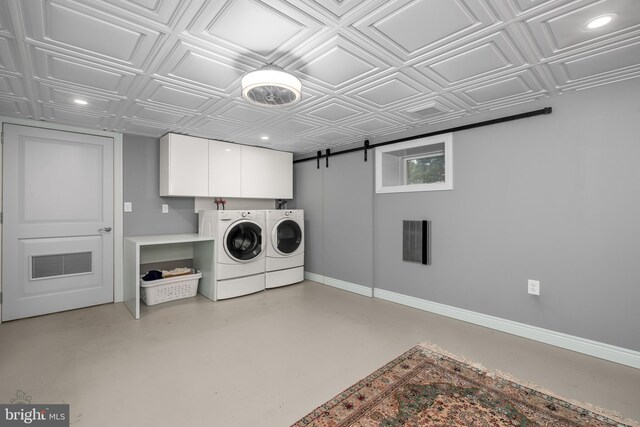 clothes washing area featuring an ornate ceiling, washing machine and clothes dryer, cabinet space, a barn door, and baseboards