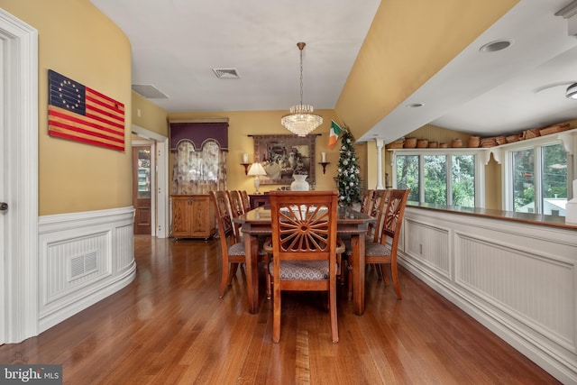 dining area with a notable chandelier, visible vents, a decorative wall, wainscoting, and wood finished floors