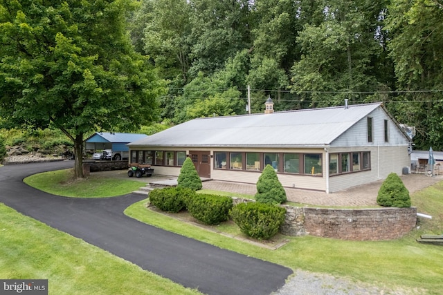 ranch-style home with aphalt driveway, metal roof, a chimney, and a front lawn