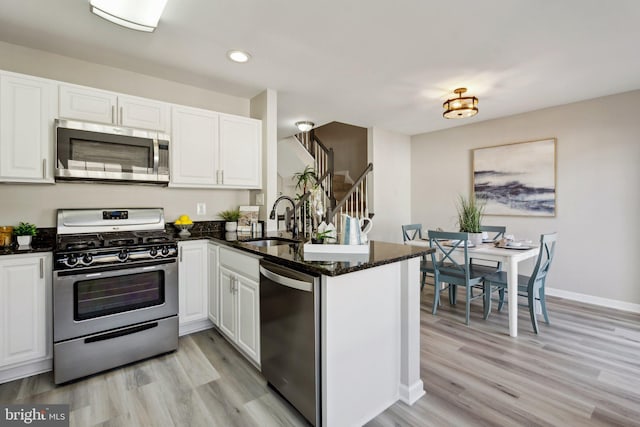 kitchen featuring stainless steel appliances, a peninsula, a sink, and white cabinets