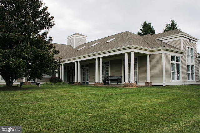 rear view of property with a shingled roof, covered porch, and a lawn