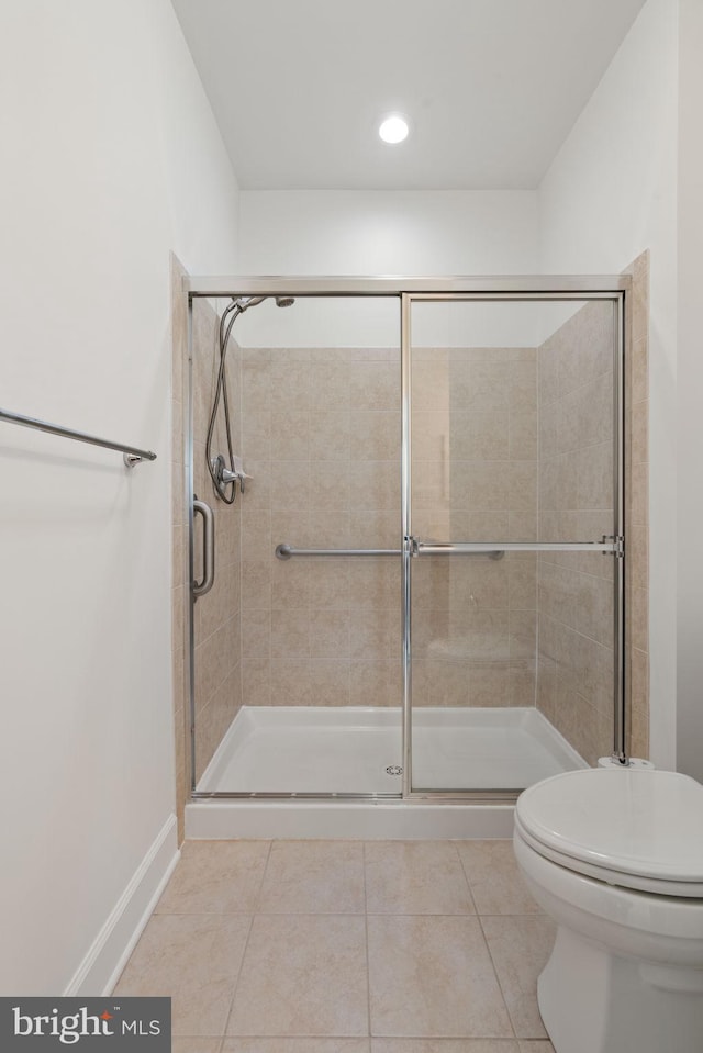 bathroom with toilet, a stall shower, baseboards, and tile patterned floors