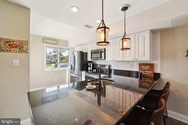 kitchen with a sink, white cabinetry, baseboards, appliances with stainless steel finishes, and pendant lighting