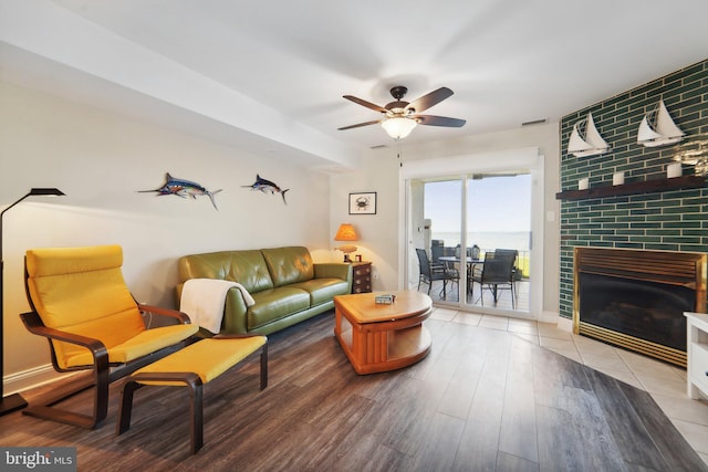 living area featuring visible vents, ceiling fan, a tiled fireplace, and wood finished floors