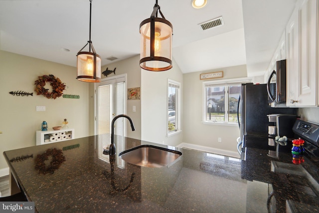 kitchen featuring visible vents, white cabinets, dark stone countertops, hanging light fixtures, and a sink