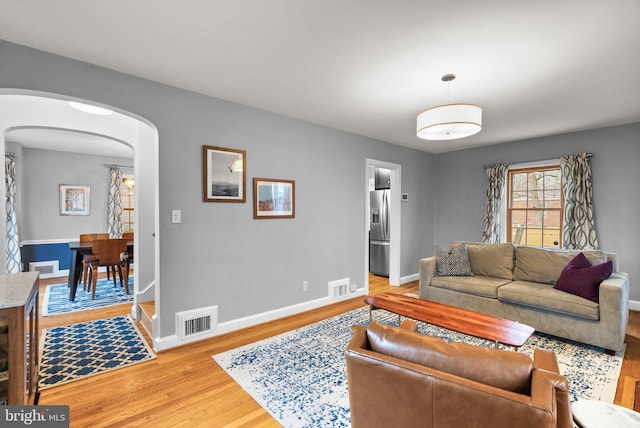 living area featuring arched walkways, light wood-type flooring, and visible vents