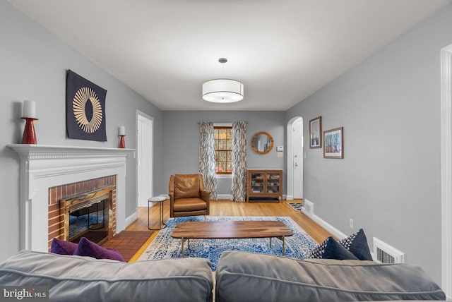 living room with a brick fireplace, visible vents, baseboards, and wood finished floors