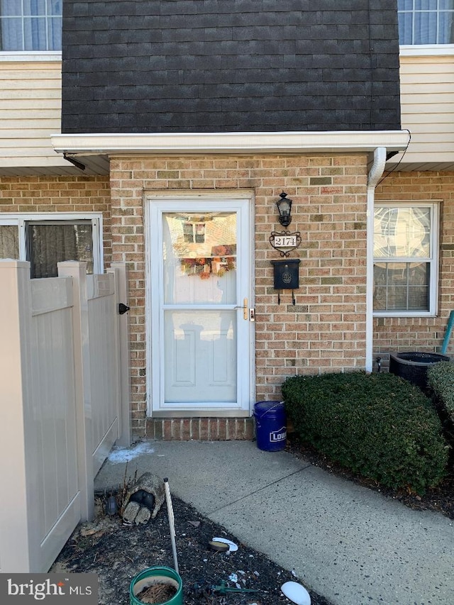 property entrance with a shingled roof, mansard roof, and brick siding