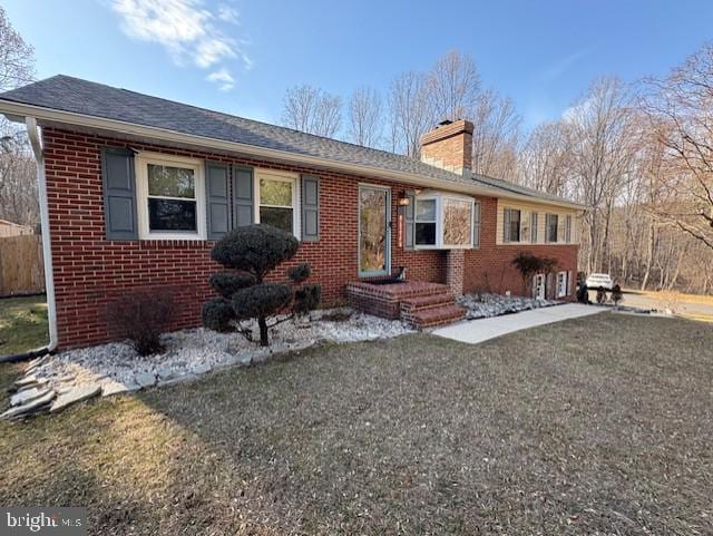 ranch-style house featuring roof with shingles, brick siding, a chimney, and a front yard