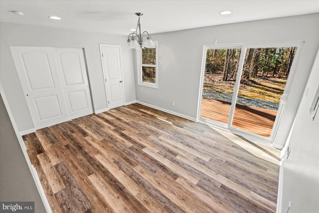 unfurnished dining area with an inviting chandelier, baseboards, wood finished floors, and recessed lighting