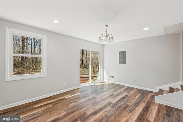 unfurnished dining area with recessed lighting, an inviting chandelier, wood finished floors, electric panel, and baseboards