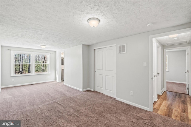 unfurnished bedroom with carpet floors, a closet, visible vents, a textured ceiling, and baseboards