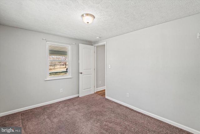 empty room featuring a textured ceiling, carpet floors, and baseboards