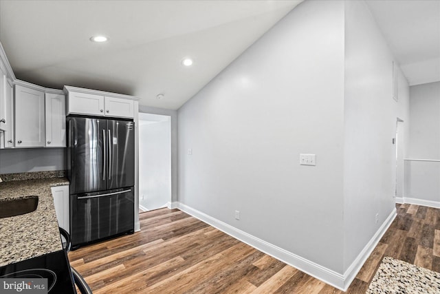 kitchen featuring wood finished floors, freestanding refrigerator, light stone countertops, vaulted ceiling, and white cabinetry