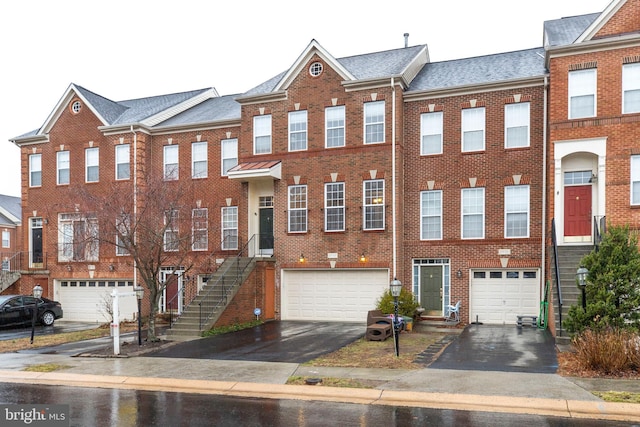 townhome / multi-family property featuring a garage, driveway, a shingled roof, and brick siding