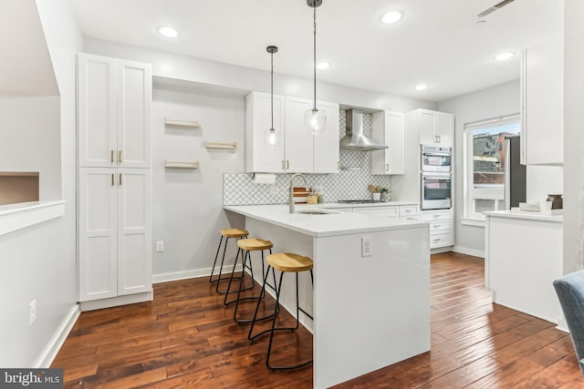 kitchen featuring a breakfast bar area, gas cooktop, a sink, white cabinetry, and wall chimney range hood