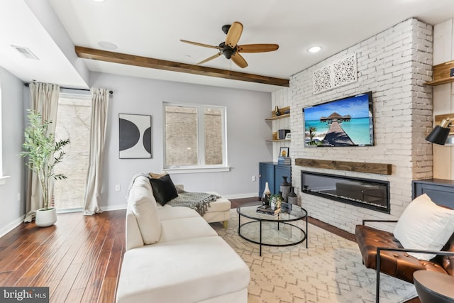 living room with a large fireplace, wood finished floors, visible vents, baseboards, and beam ceiling