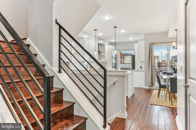 stairway with a notable chandelier, a city view, recessed lighting, wood finished floors, and baseboards