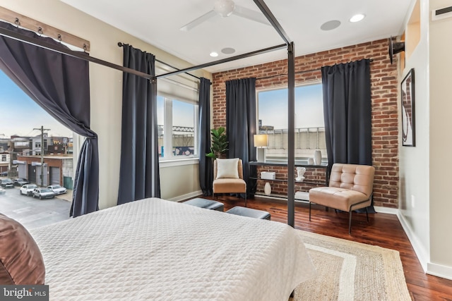 bedroom with brick wall, wood finished floors, visible vents, and baseboards