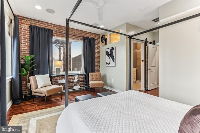 bedroom featuring wood finished floors, visible vents, brick wall, and a barn door