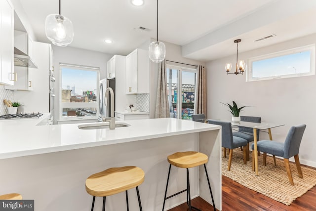 kitchen with light countertops, a sink, a peninsula, and wall chimney exhaust hood