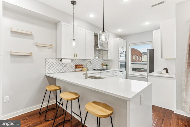 kitchen with visible vents, dark wood-style flooring, a sink, wall chimney range hood, and backsplash