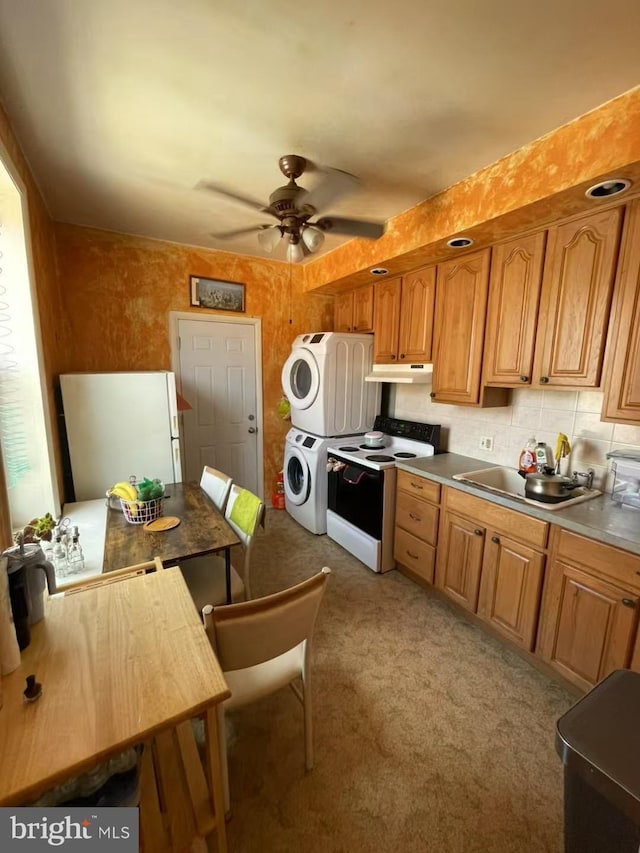 kitchen featuring under cabinet range hood, a sink, electric stove, brown cabinetry, and stacked washer and clothes dryer