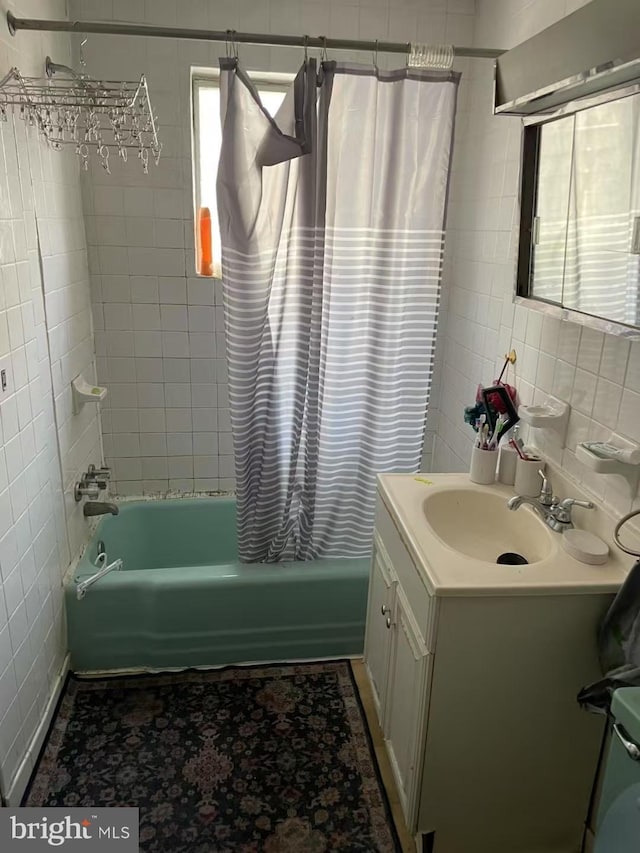 bathroom with a healthy amount of sunlight, shower / bathtub combination with curtain, tile walls, and vanity