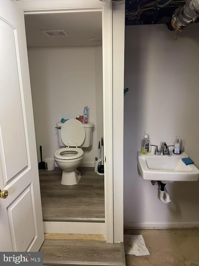 bathroom with toilet, a sink, wood finished floors, and visible vents