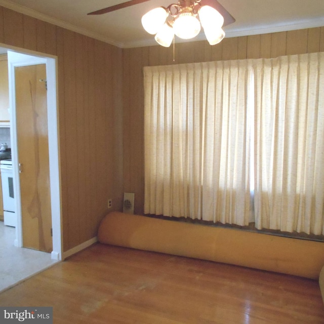 spare room with a ceiling fan, crown molding, wooden walls, and wood finished floors