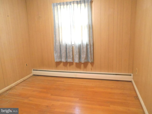 spare room featuring baseboards, baseboard heating, wood finished floors, and wooden walls