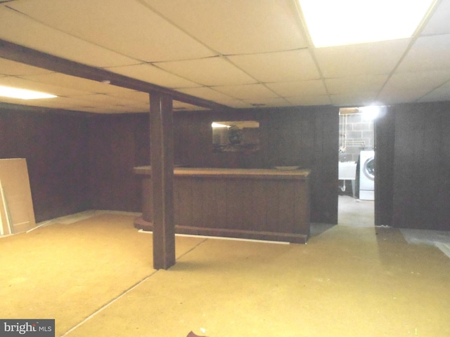 finished basement with a paneled ceiling, washer / clothes dryer, a sink, and a bar