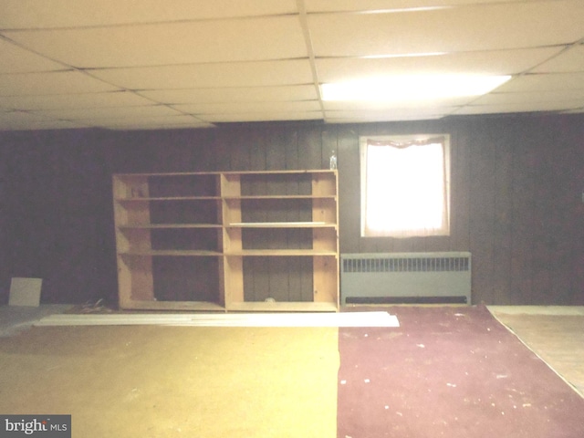 basement with a paneled ceiling and radiator