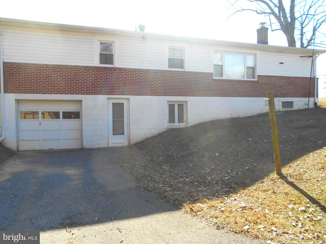 exterior space with a garage, brick siding, driveway, and a chimney