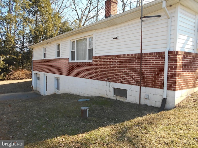 view of side of home featuring brick siding, a yard, a chimney, and an attached garage