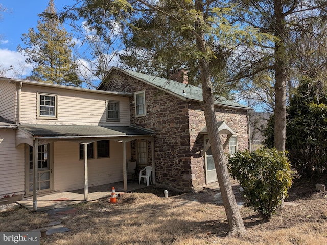 exterior space with stone siding, a chimney, and a patio