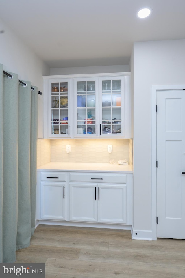 interior space with glass insert cabinets, light countertops, white cabinetry, and decorative backsplash