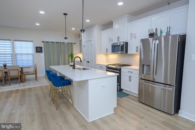 kitchen featuring an island with sink, appliances with stainless steel finishes, light countertops, white cabinetry, and a sink