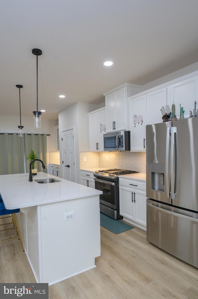 kitchen with decorative light fixtures, a center island with sink, light countertops, appliances with stainless steel finishes, and a sink