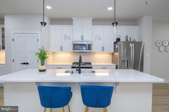 kitchen with light countertops, appliances with stainless steel finishes, a center island with sink, and decorative light fixtures