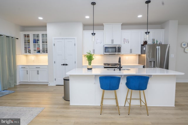 kitchen featuring a center island with sink, glass insert cabinets, stainless steel appliances, and pendant lighting