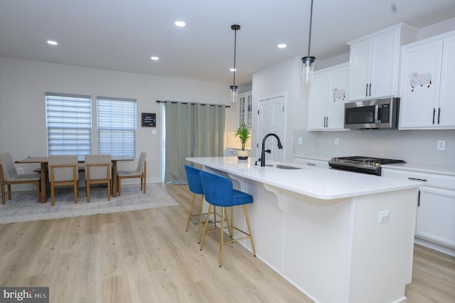 kitchen featuring stainless steel appliances, a sink, white cabinets, light countertops, and a center island with sink