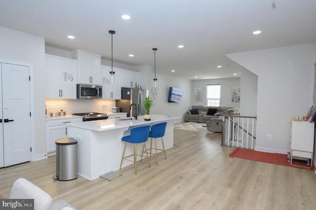 kitchen with white cabinets, an island with sink, open floor plan, stainless steel appliances, and light countertops