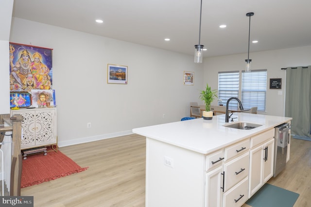 kitchen featuring pendant lighting, a center island with sink, light countertops, stainless steel dishwasher, and a sink