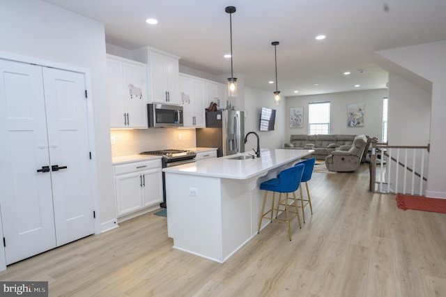 kitchen featuring a sink, open floor plan, light countertops, appliances with stainless steel finishes, and a center island with sink